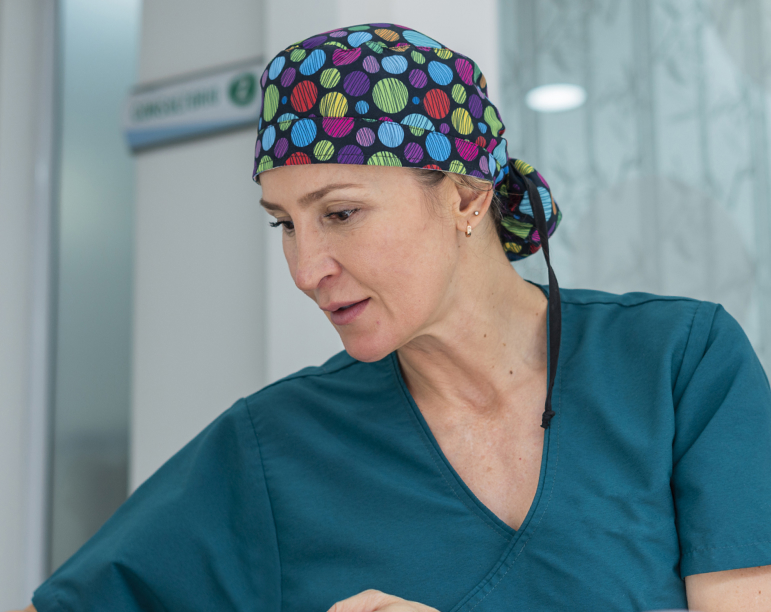Female breast surgeon in surgical cap interacts with unseen patient. 
