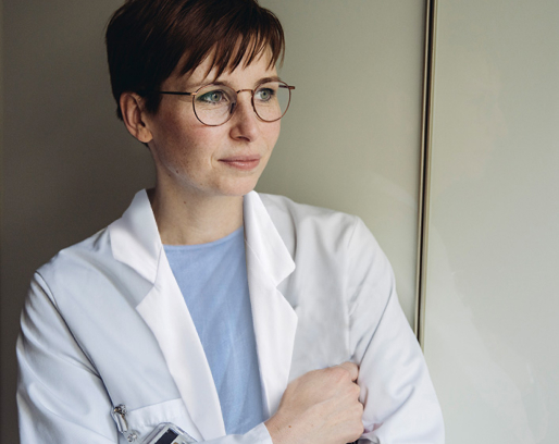 Female medical oncologist leans against wall as she pauses in thought. 