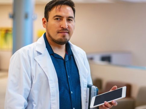 Male medical oncologist pauses work on a small tablet, looking at the camera. 